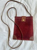 Full view of red suede pouch purse with long brown leather strap