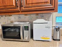 Microwave, bread maker and can opener grouped on countertop