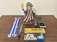 Group shot of all six items on table: luminary, radio, bell, letter opener, bar magnifier box, lighted magnifier box