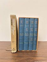 Calculus textbook with worn dust jacket beside slipcased four-volume blue cloth set