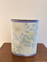 Front view showing floral metal wastebasket with lavender trim, dent on rim