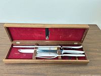 Open walnut box showing sharpening steel, carving knife, carving fork in red felt interior