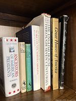 Spines of seven hardcover books on shelf showing titles and dust jackets