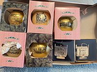 Box with four gold glass ornaments and three black-case metal ornaments inside shipping carton
