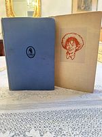 Blue hardcover book closed alongside tan book opened to illustrated frontispiece