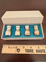 Four miniature silver-plated shakers in blue felt-lined box beside ruler for scale