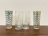 Six highball tumblers: two patterned with blue, turquoise and gold wave design and four plain clear glasses