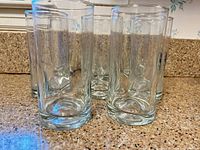 Eight clear cylindrical highball glasses on countertop