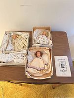 Three dolls in open boxes with tissue and pamphlet on table