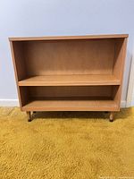 Front view of light brown wood veneer bookcase showing two shelves and legs