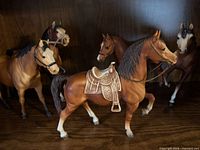 Group of five plastic horse figurines, front one with ornate saddle