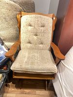 Front view of one glider rocker showing wood frame, beige tufted back cushion, seat cushion