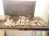 Overview of assorted flatware pieces laid out on table with glass serving tray visible