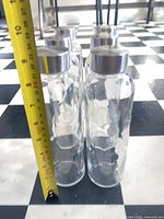 Six clear glass bottles with metal lids beside measuring tape