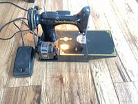 Full view of Singer sewing machine with light on, foot pedal and cords visible