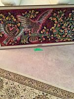 Full view of framed needlepoint panel leaning against sofa, shows birds, foliage and frame