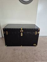 Front view of black metal steamer trunk showing brass hardware