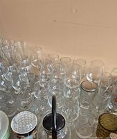 Multiple rows of clear glass stemware and a glass teapot among smaller bowls