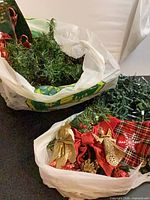 Two plastic bags containing green garland, red ribbons, gold bows, and gold glitter ornaments