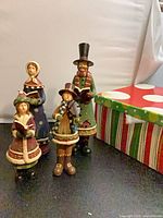 Four resin caroler figurines and striped box