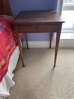 Full view of table beside bed showing drawer and legs