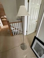 Full view of metal floor lamp showing pole, base, shade, cord