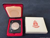 Coin in mount inside open case alongside sleeve