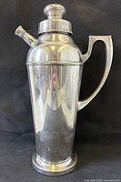 Full view of silver-plated cocktail shaker showing handle, spout, lid and foot