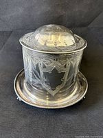 Front view of silver plated biscuit barrel showing engraved shield cartouche and domed lid