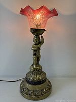 Full view of bronzed cherub lamp illuminated with cranberry glass shade
