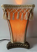 Front view lit showing fabric shade, tassel fringe and metal base