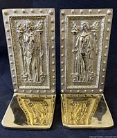 Front view of both brass bookends showing relief figures and rivet border
