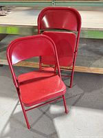 Two red metal folding chairs standing folded and partially unfolded