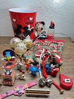 Overall lot overview showing bucket, plush, water bottle, ornaments, mittens, bells, figurines, bracelet, toy camera