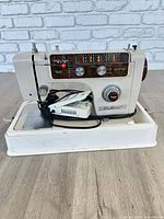 Front view of Fleetwood sewing machine showing control panel, knobs, logo, foot pedal and plastic base