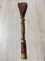 Full view of war club showing entire length, leather head, twine wraps, metal studs