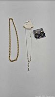 All three jewellery items laid out: gold chain, silver rhinestone necklace on card, black hoop earrings on card