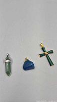 Overview of three pendants laid out: green point, blue stone, malachite cross