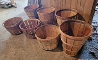 Seven wooden bushel baskets grouped on floor showing exterior bands and slat construction