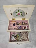 open jewelry box showing upper compartment with rings, earrings, brooches and lower drawer with faux pearls