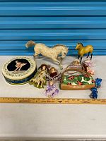 Group shot of all items including horses, dolls, tin, purse, and blue bears with ruler for scale