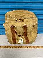 Full view of canvas aviation bag with leather handles, attached tag and ruler for scale, manufacturer label visible