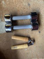 Two chrome dumbbells and Everlast hand grip on wooden floor