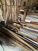 Overall view of stacked lumber pieces of different sizes on floor and against wall