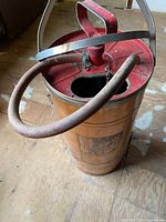 Full view of cylindrical sprayer showing red lid, pump, handle and hose