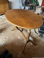 Full view of oval wooden tilt-top table standing on tripod base