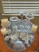 Top view showing all 10 clear crystal and glass candle holders on round glass table, varying heights and styles