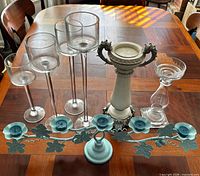 Front view showing all seven candle holders including four clear glass hurricanes, one white resin pillar, one clear glass pillar, and one teal vine tea-light holder