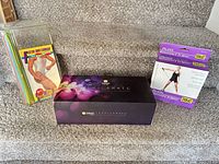 All three exercise sets displayed on stairs: Zumba Exhilarate box centred, Flatten Your Stomach band set left, Everlast Pilates tubing box right