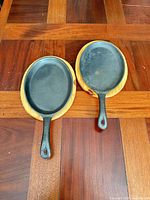 Two cast iron oval skillets on matching wooden bases